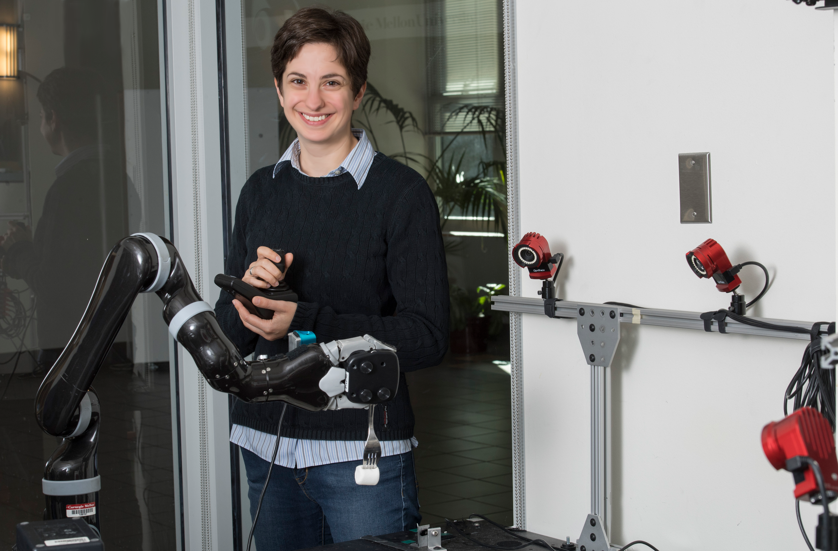Professor Admoni holding a joystick next to a black robot arm